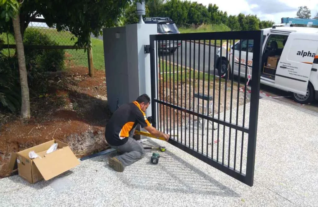 Technician repairing a black automatic swing gate at a residential driveway.