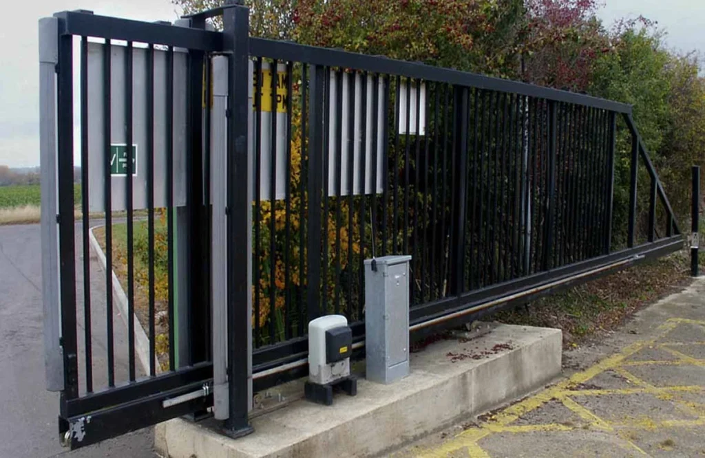  Black automatic sliding gate with motor and control box beside a roadway entrance.
